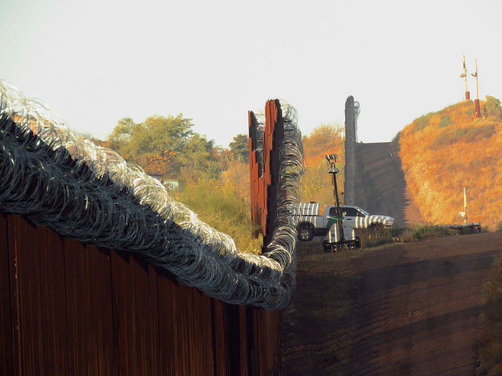 Looking down the border wall, with a pickup truck in the distance