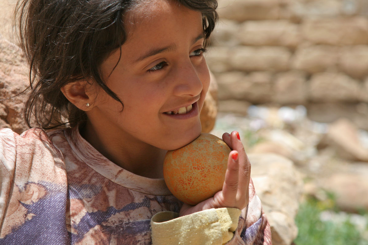 A child smiles while holding a ball and looking into the distance.