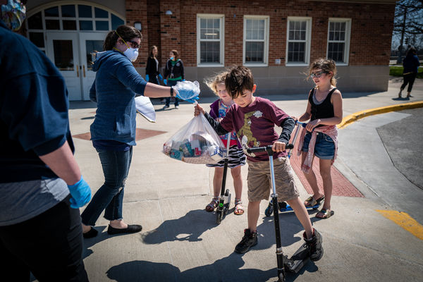 Des Moines Public Schools launched a huge increase in the number of free meal sites for students during the COVID-19 closure, going from 22 to 50 locations around the city. Here students on scooters receive a bag of food from volunteers.